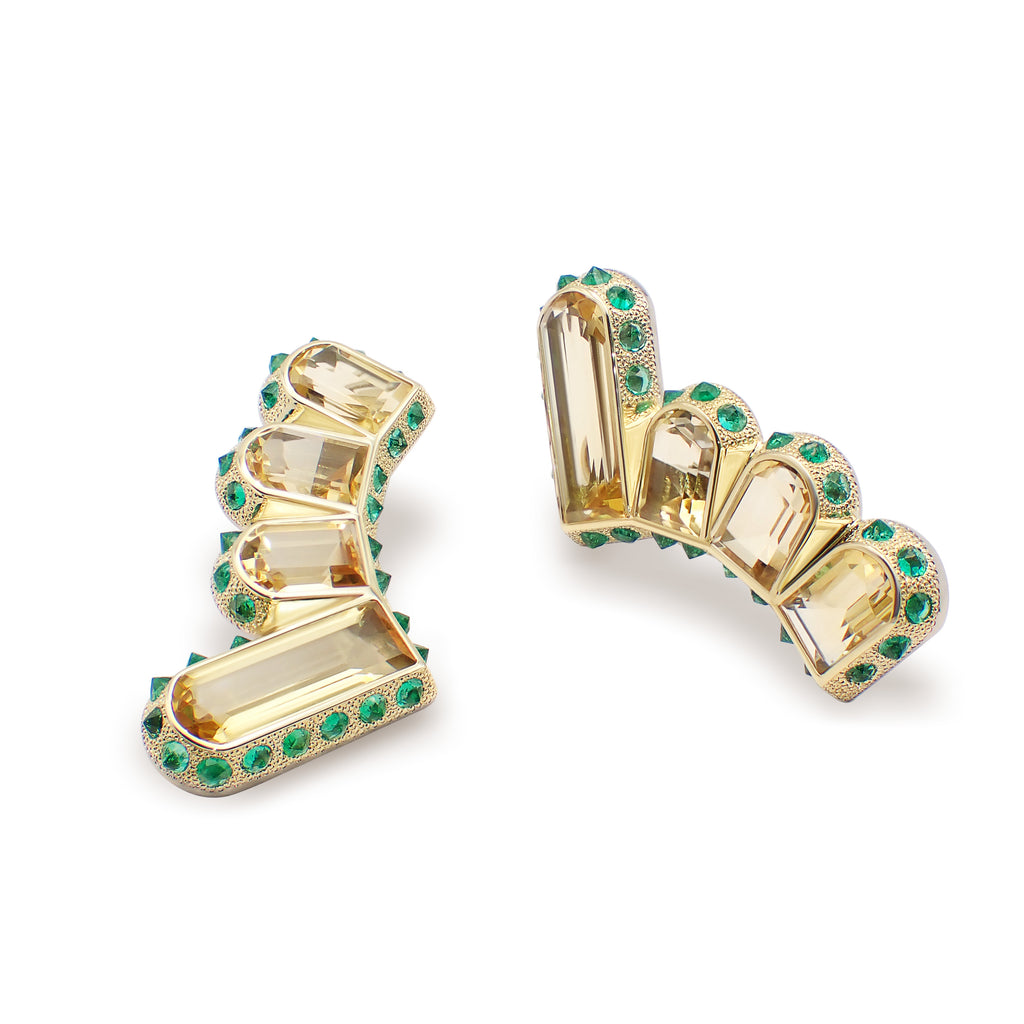 A pair of earrings featuring elongated rectangular citrines surrounded by round emeralds set in gold. Hyperborea Earrings by Hugo Cahill featuring elongated rectangular citrines and an emerald halo
