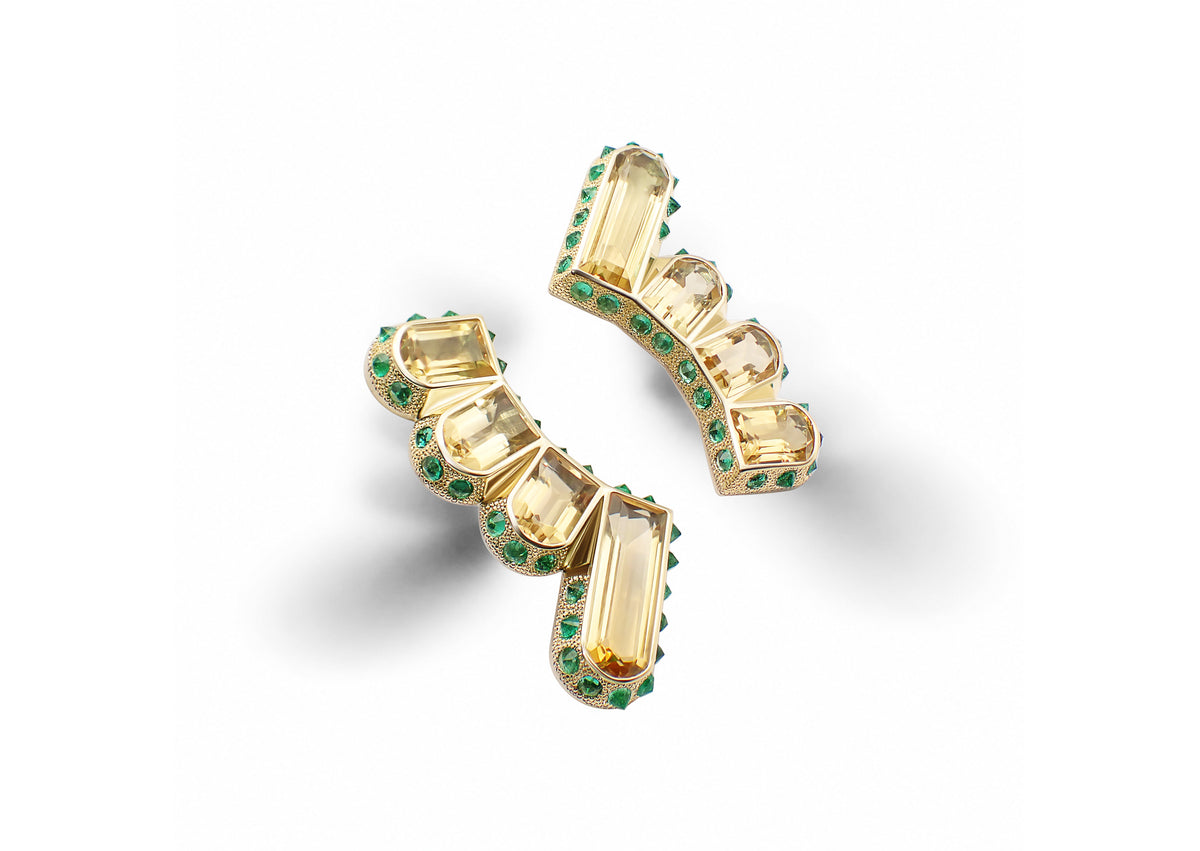 Hyperborea Earrings shown at an angle, the elongated citrines framed by reverse-set emeralds within a textured gold architecture.